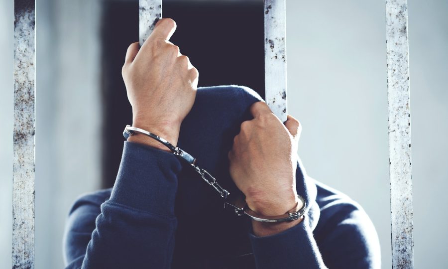 Handcuffed hands of a prisoner behind the bars of a prison with blue clothes